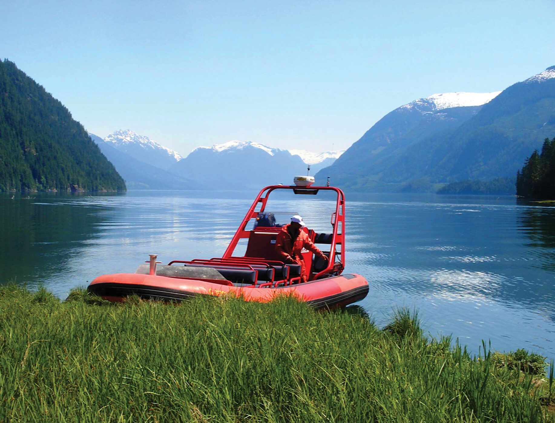 Rode hovercraft op een grasrijke oever bij een kalm meer met bergen op de achtergrond.