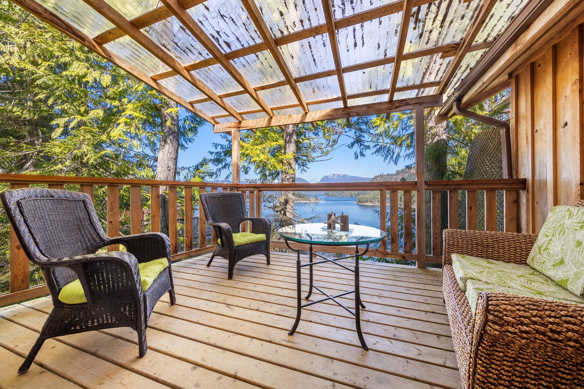 Houten terras met rieten stoelen, tafel en uitzicht op de oceaan onder een pergola.