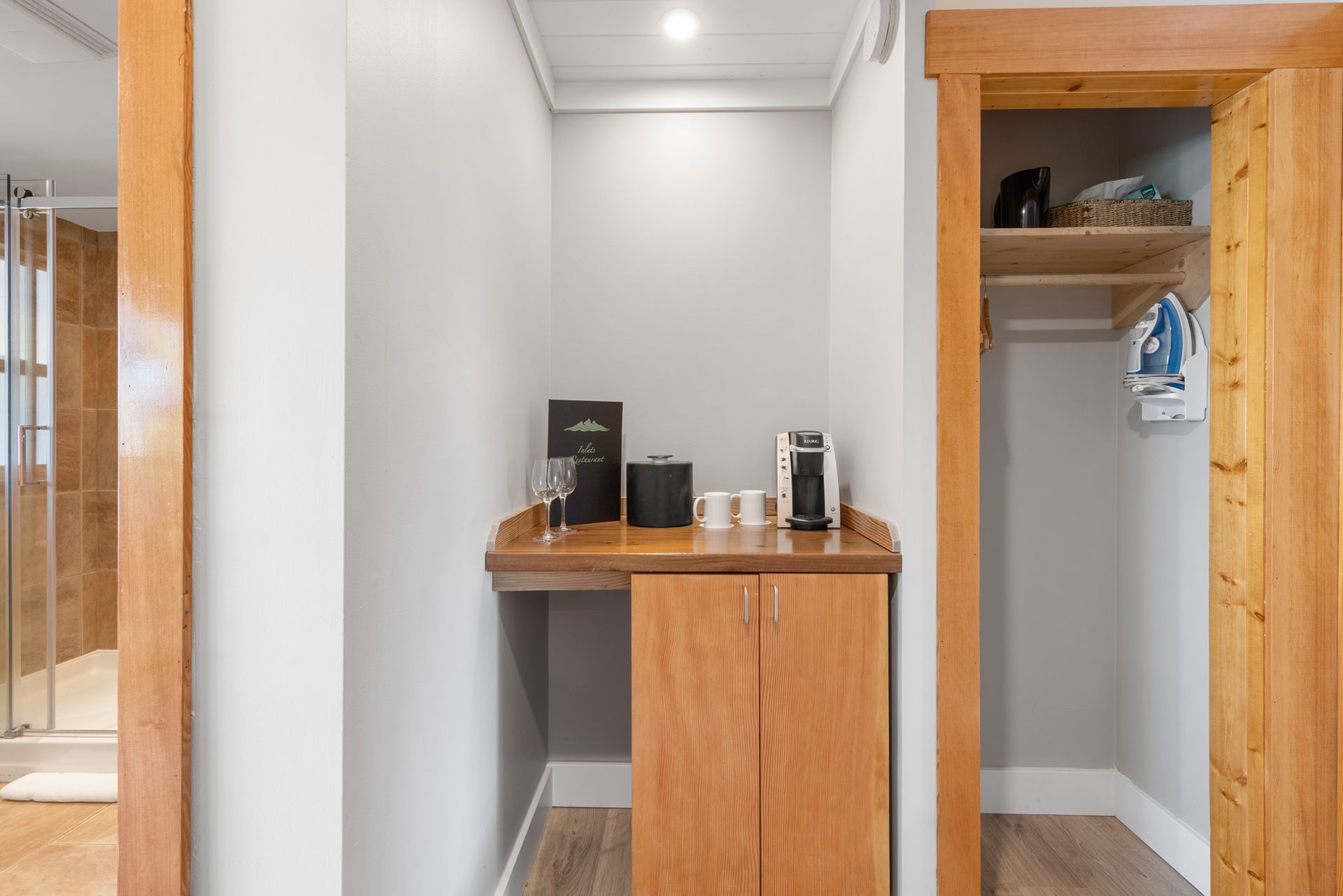 Compacte kastnis met een houten bureau, planken en hangende kleding in een witte gang.