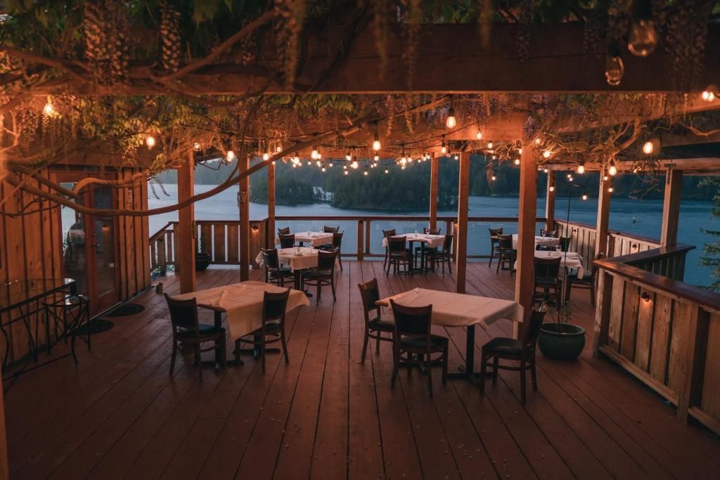 Een sfeervol verlicht terras bij schemering met lege tafels, stoelen, lichtslingers en uitzicht op het water.