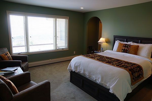 Hotelkamer met een opgemaakt bed, stoelen en een groot raam met uitzicht over de stad.