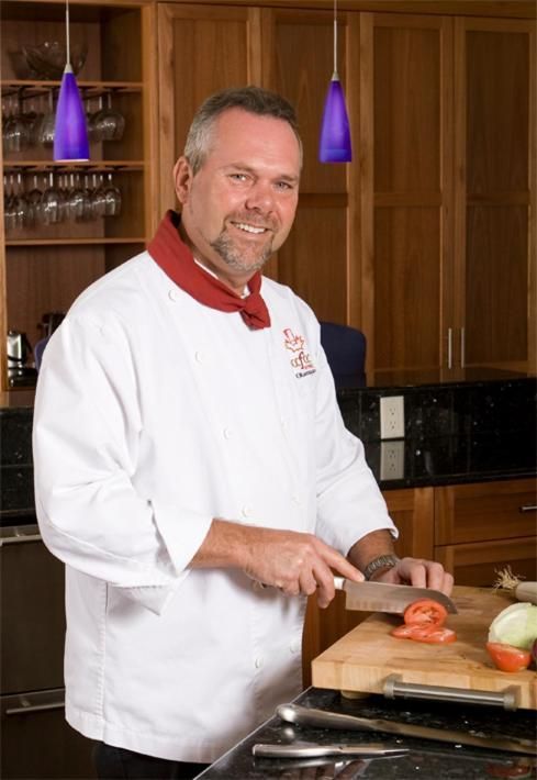 Een chef-kok snijdt tomaten in een keuken, staand naast houten kasten en paarse hanglampen.