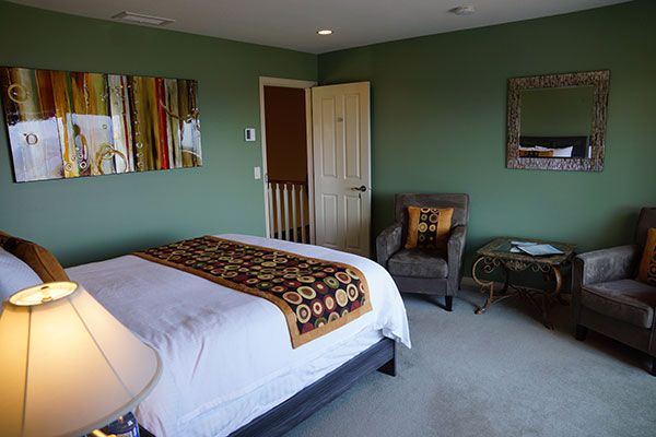 Moderne slaapkamer met groene muren, witte sprei, een loper met patroon en een zithoek bij een spiegel.