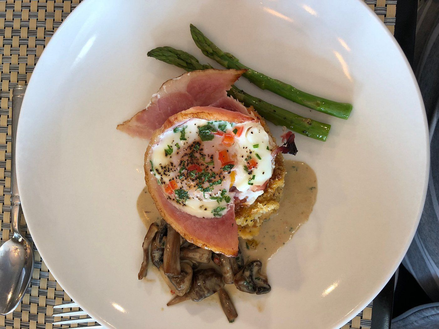 Een prachtig opgemaakt eiergerecht met asperges, kruiden en champignons, geserveerd op een wit bord.