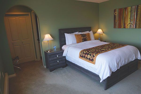 Gezellige slaapkamer met een kingsize bed, nachtlampjes, groene muren en een boogvormige deuropening.