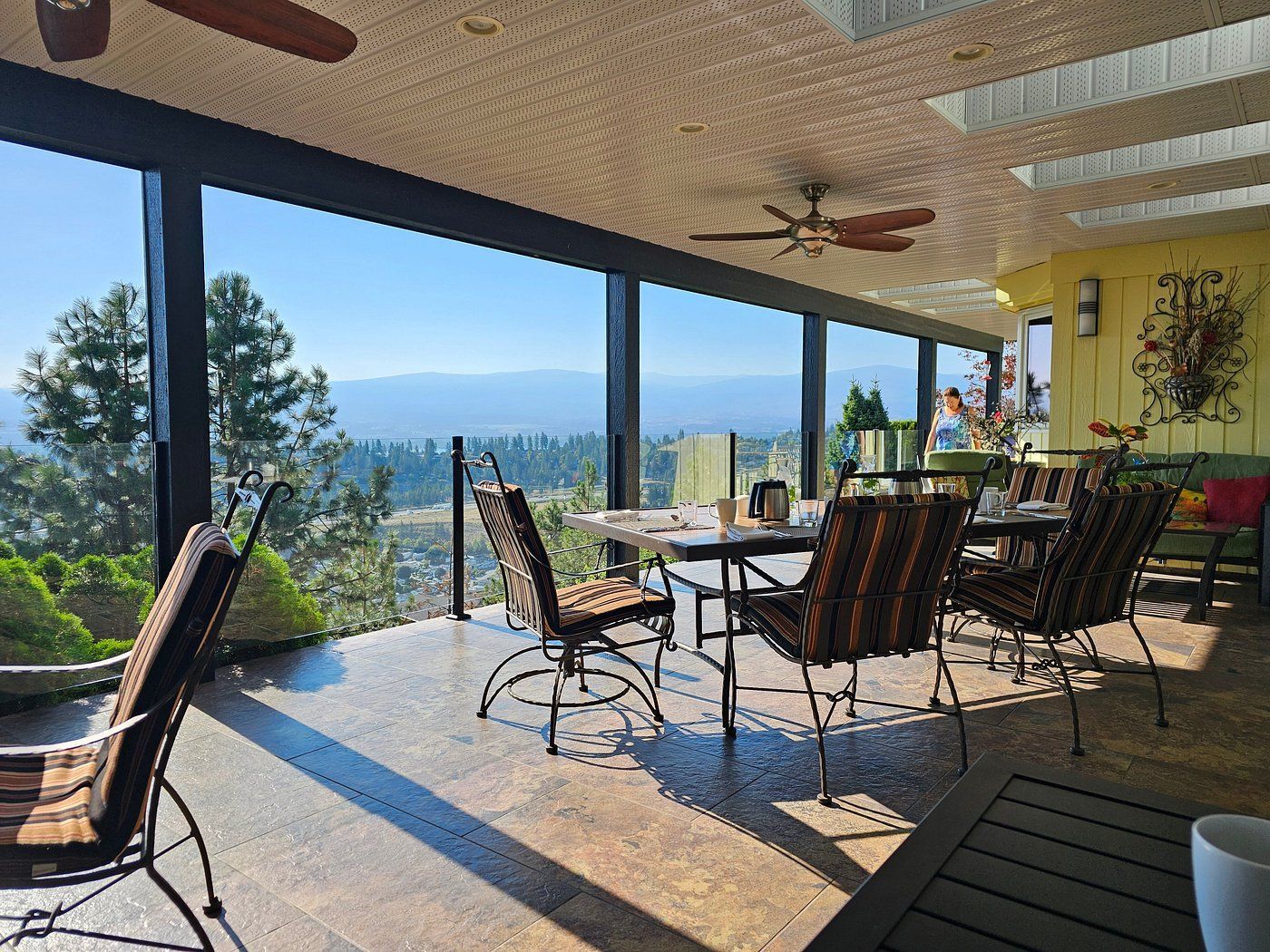 Overdekt terras met stoelen en tafels met uitzicht op een zonnig berglandschap.