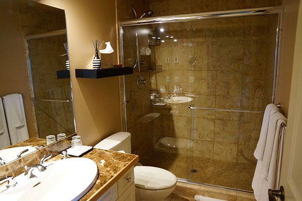 Moderne badkamer met glazen douchecabine, marmeren wastafel en toilet op een beige tegelvloer.