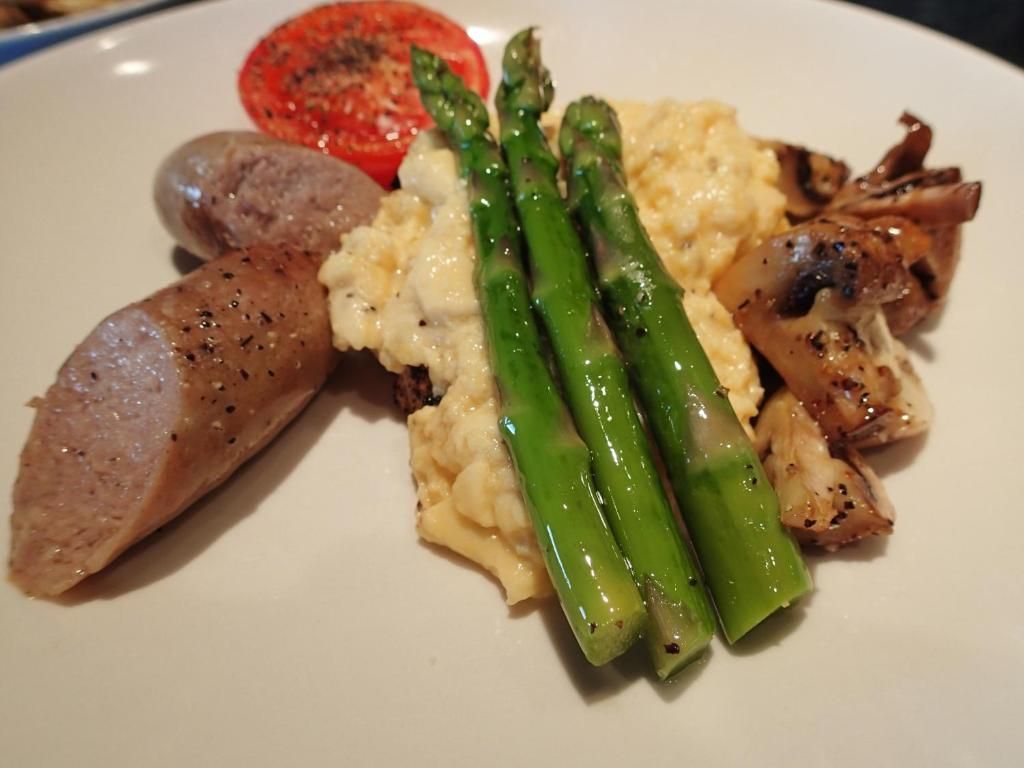 Een rijkgevulde gastronomische maaltijd met asperges, aardappelpuree, plakjes worst, tomaat en champignons.