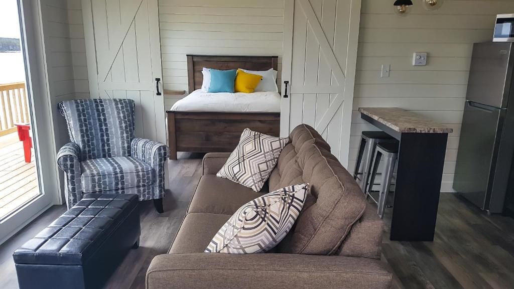 Gezellige overdekte veranda met een bruine bank, een gestreepte fauteuil, een bed en een zwart bijzettafeltje op een houten vloer.