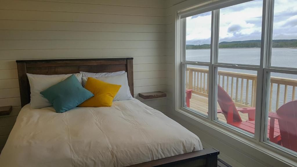 Gezellige slaapkamer met een bed, turquoise en gele kussens en uitzicht op rode stoelen op een terras.
