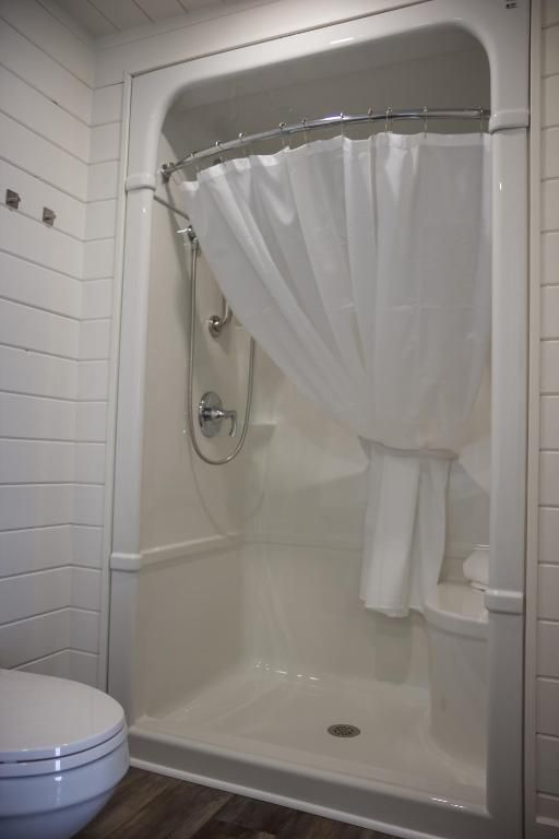 Witte douchecabine met gordijn in een kleine badkamer, met links een gedeeltelijk zichtbaar toilet.