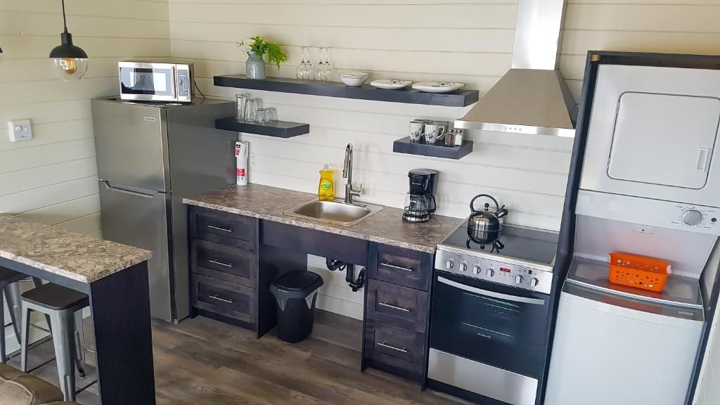 Kleine, moderne keuken met roestvrijstalen koelkast, fornuis, spoelbak, donkere kasten en open planken.