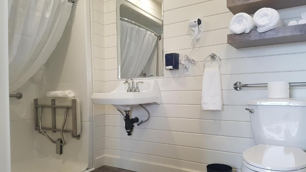 Kleine badkamer met witte wastafel, toilet, douchegordijn, handdoeken en wandplanken.