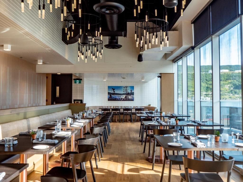 Moderne restaurantzaal met gedekte tafels, houten stoelen en ramen van vloer tot plafond met uitzicht op het water.