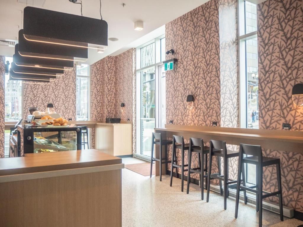 Modern café-interieur met barkrukken, hanglampen en behang met een patroon langs de hoge ramen.