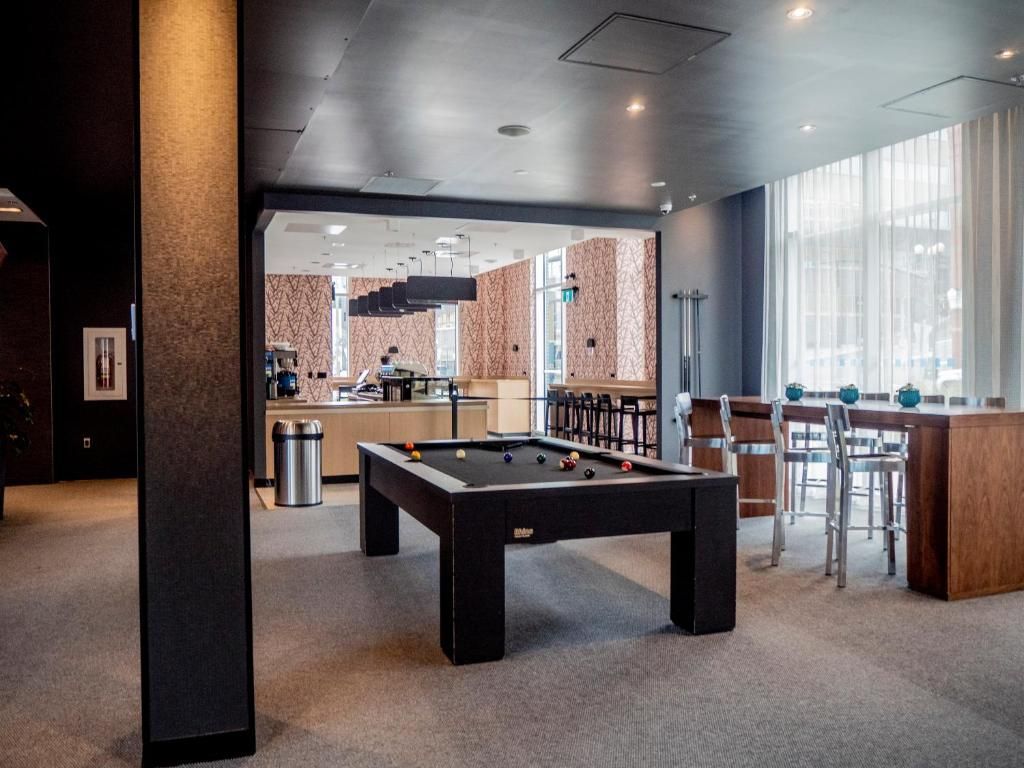 Moderne lounge met een pooltafel, barkrukken en grote ramen in een kamer met bakstenen accenten.