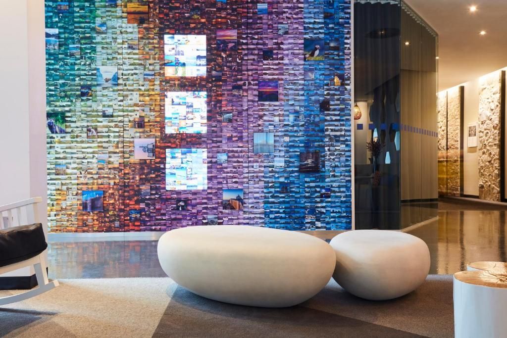 Moderne lobby met een kleurrijke mozaïekwand en twee witte ovale banken onder warme verlichting.