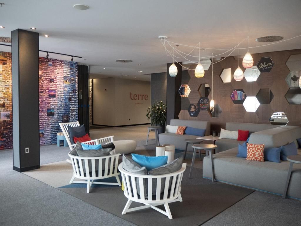 Moderne hotellobby met grijze zitmeubels, witte stoelen, hanglampen en zeshoekige wanddecoratie.
