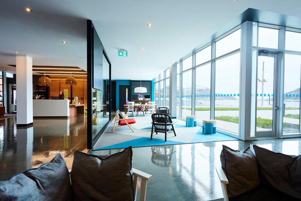 Moderne lounge met grote ramen, glanzende vloeren en kleurrijke stoelen met uitzicht op het water.