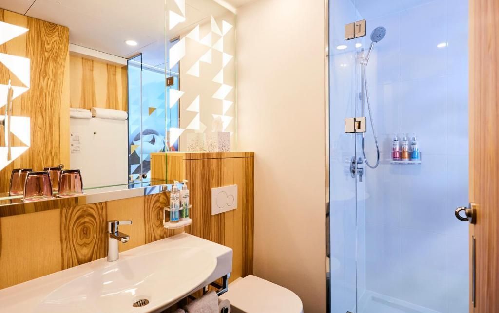 Moderne badkamer met witte wastafel, houten accenten, spiegel en blauwe glazen douchedeur.