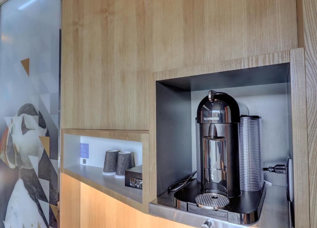 Koffiehoek met een zilverkleurige espressomachine en een stapel transparante kopjes in een houten nis.