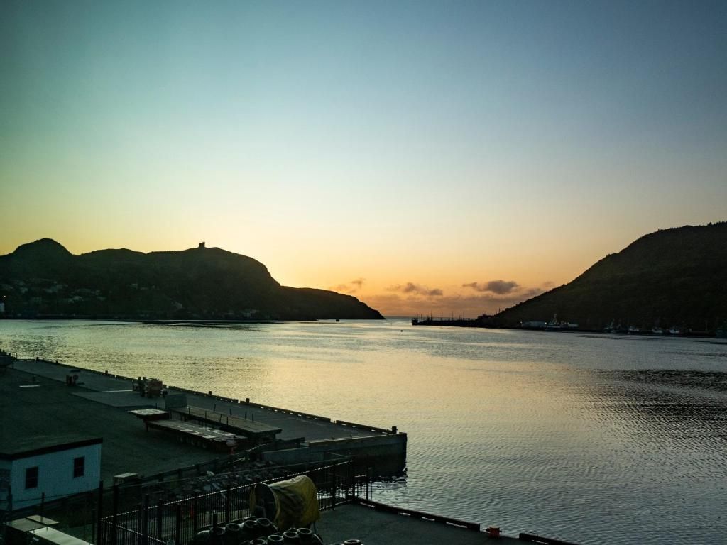Zonsondergang boven een kalme haven met silhouetten van heuvels en een pier op de voorgrond.