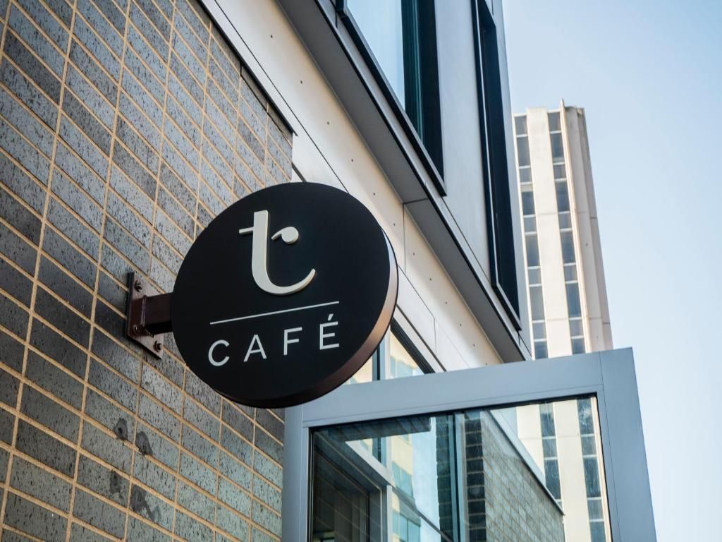 Rond zwart cafébord op de gevel van een gebouw met glazen ramen en een hoge toren op de achtergrond.