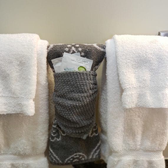 Een opgerolde grijze doek, gecentreerd tussen twee witte handdoeken op een beige ondergrond.