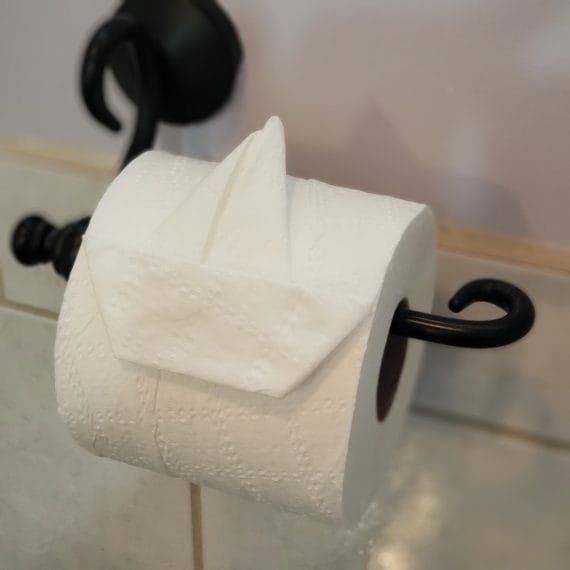 Een rol toiletpapier op een zwarte wandhouder met een velletje eroverheen gevouwen.