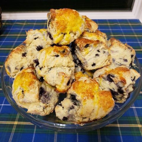 Een glazen schaal gevuld met bosbessenscones op een blauw geruit tafelkleed.