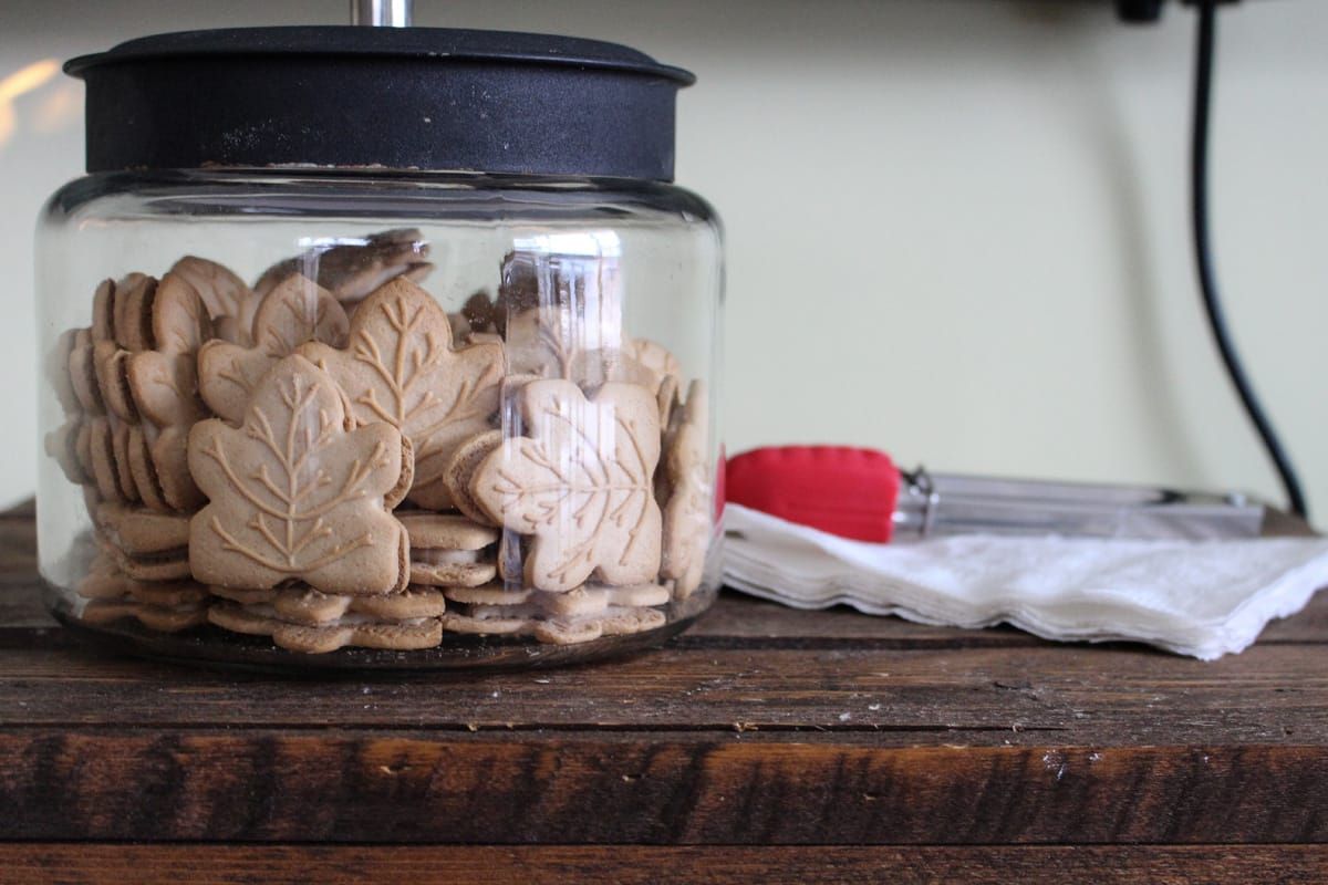 Glazen pot met houten hartvormige stukjes op een donkere plank naast een rood-wit tafelkleed.