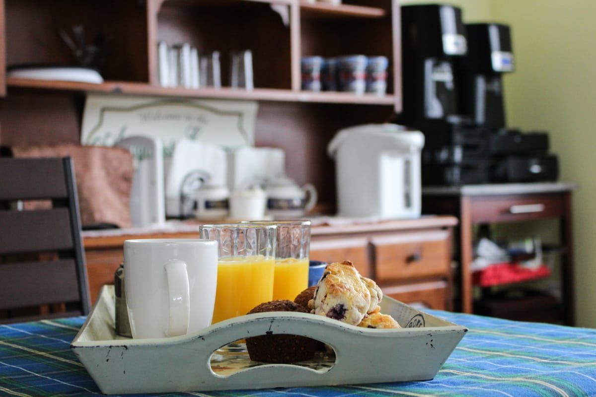 Ontbijtplateau met koffie, sinaasappelsap en gebak op een blauw tafelkleed in een keuken.