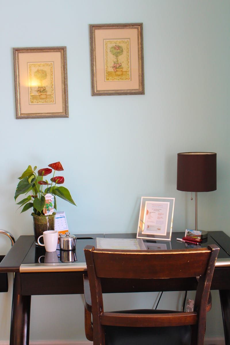 Een bureau voor thuiswerk met stoel, lamp, ingelijste kunst en een potplant tegen een lichtblauwe muur.
