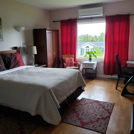 Slaapkamer met rode gordijnen, een bed, kledingkast, uitzicht door het raam en een bureaustoel op een houten vloer.