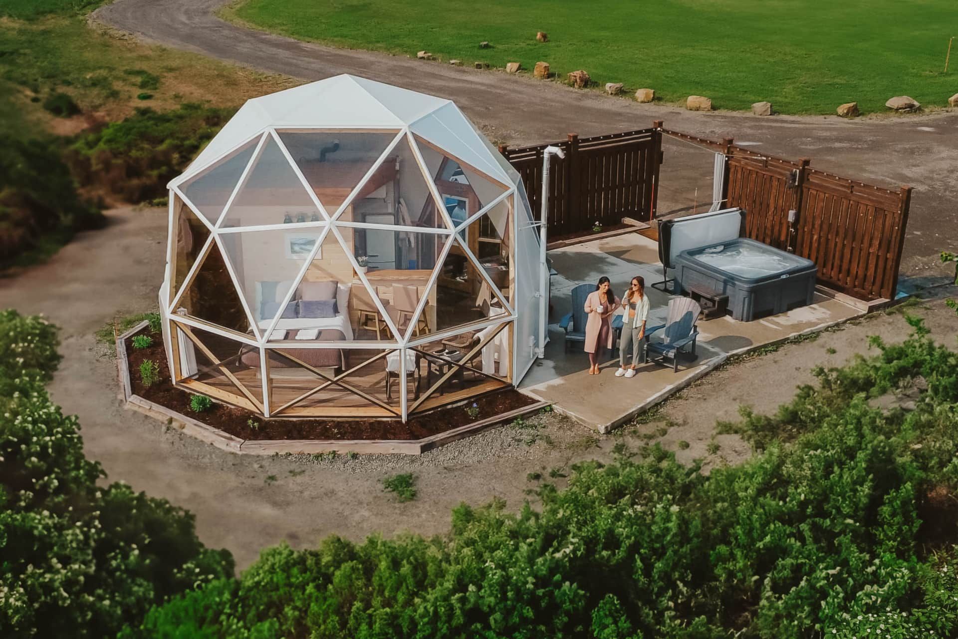 Een dome van Appalaches Domes met mensen buiten op een landelijk, onverhard terrein, omgeven door groene velden.