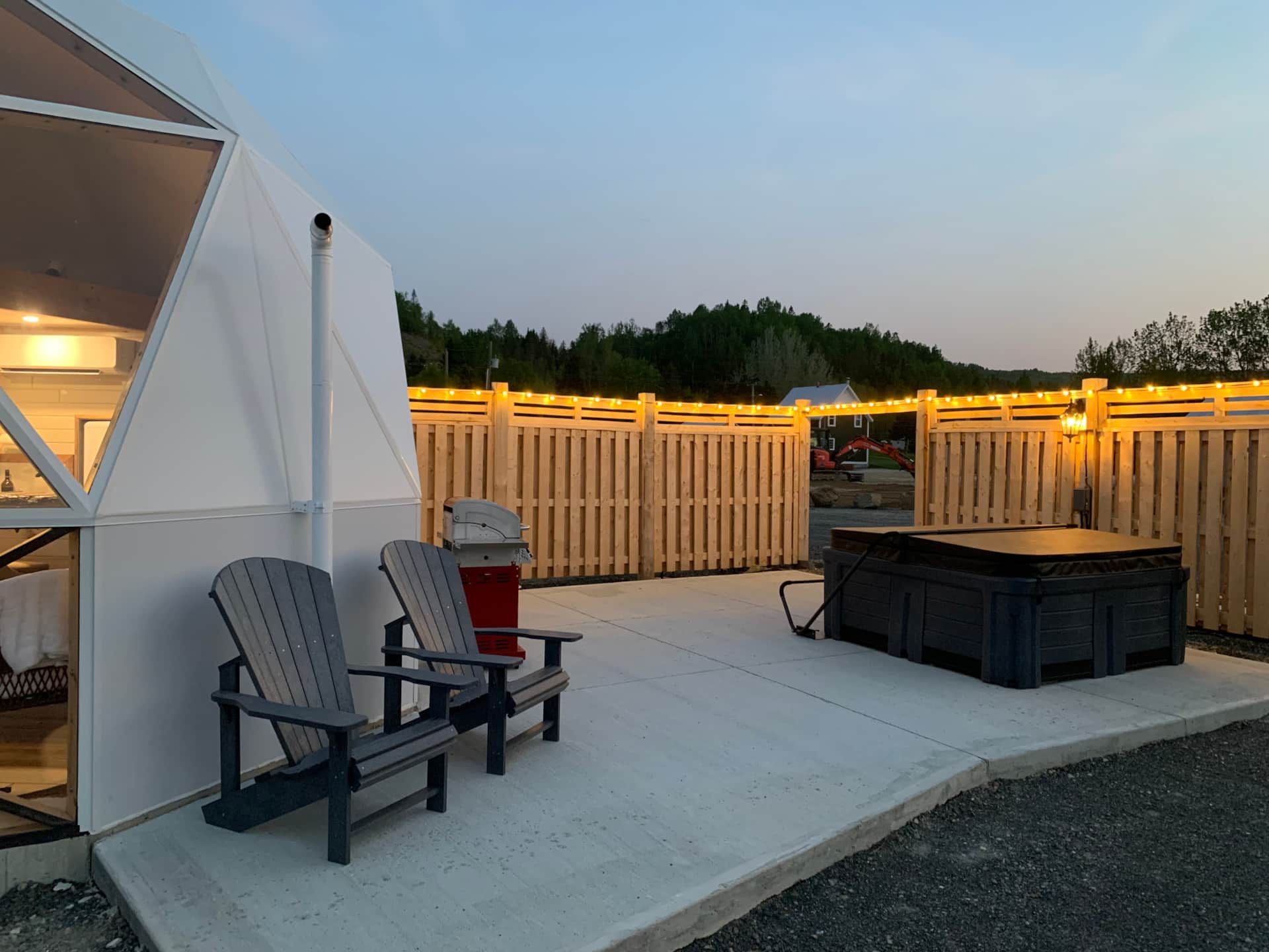 Terras met twee stoelen, een jacuzzi, een witte schutting en sfeervolle lichtslingers bij schemering.