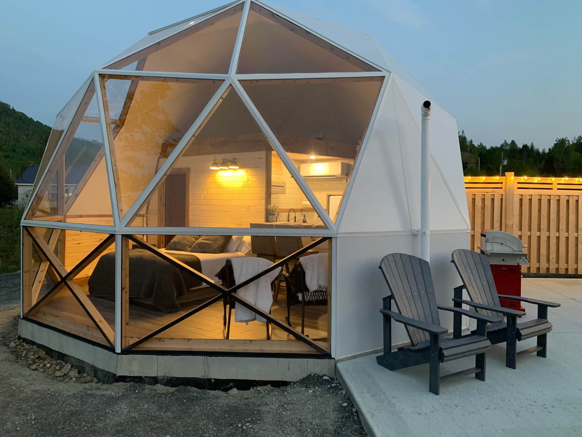 Geodetische dome van Appalaches Domes 's nachts verlicht met stoelen op een terras buiten.