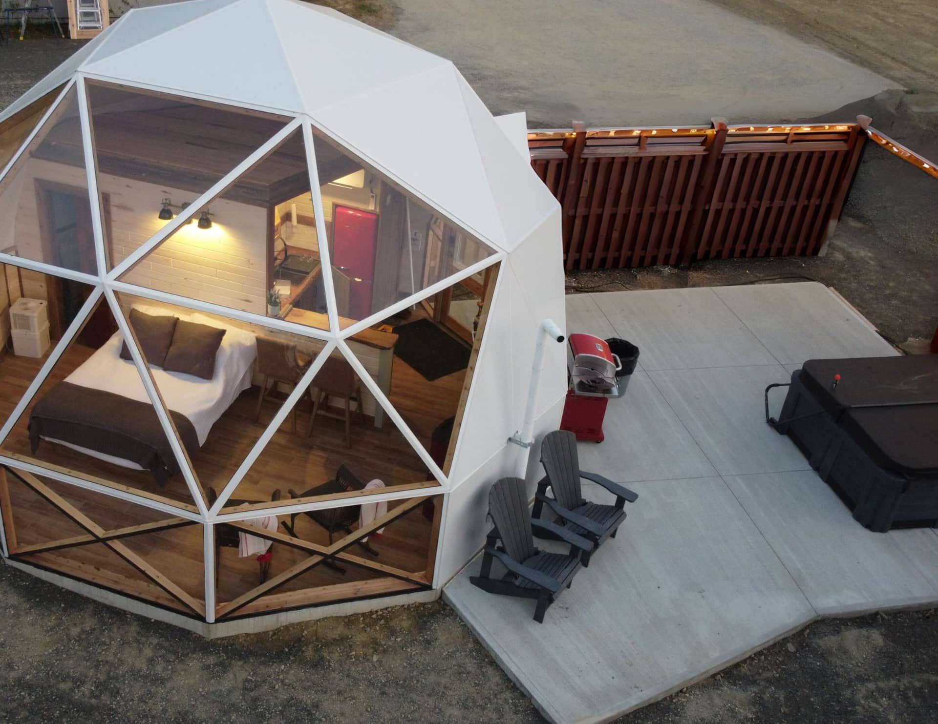 Geodetische koepeltent van Appalaches Domes voor glamping op een terras met ligstoelen en uitzicht op het water.