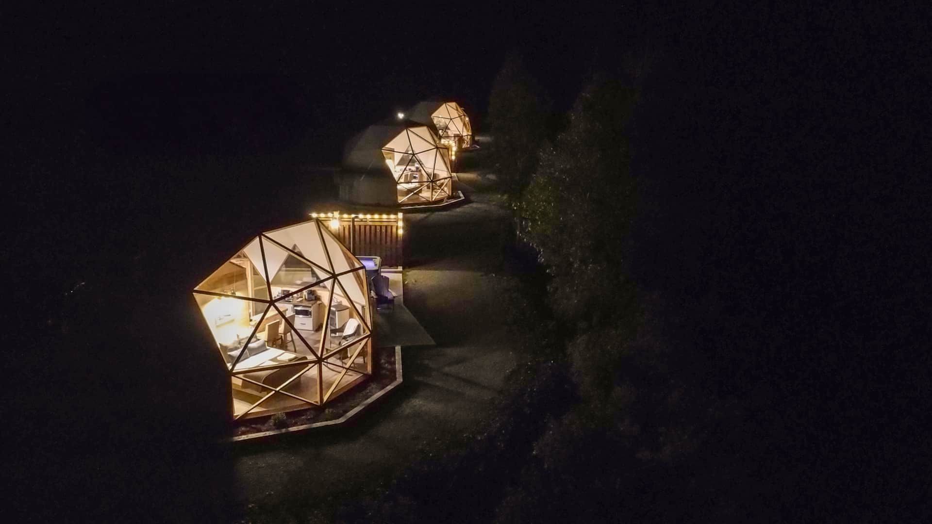 Warm verlichte geometrische domes van Appalaches Domes 's nachts langs een donker, kronkelend pad.