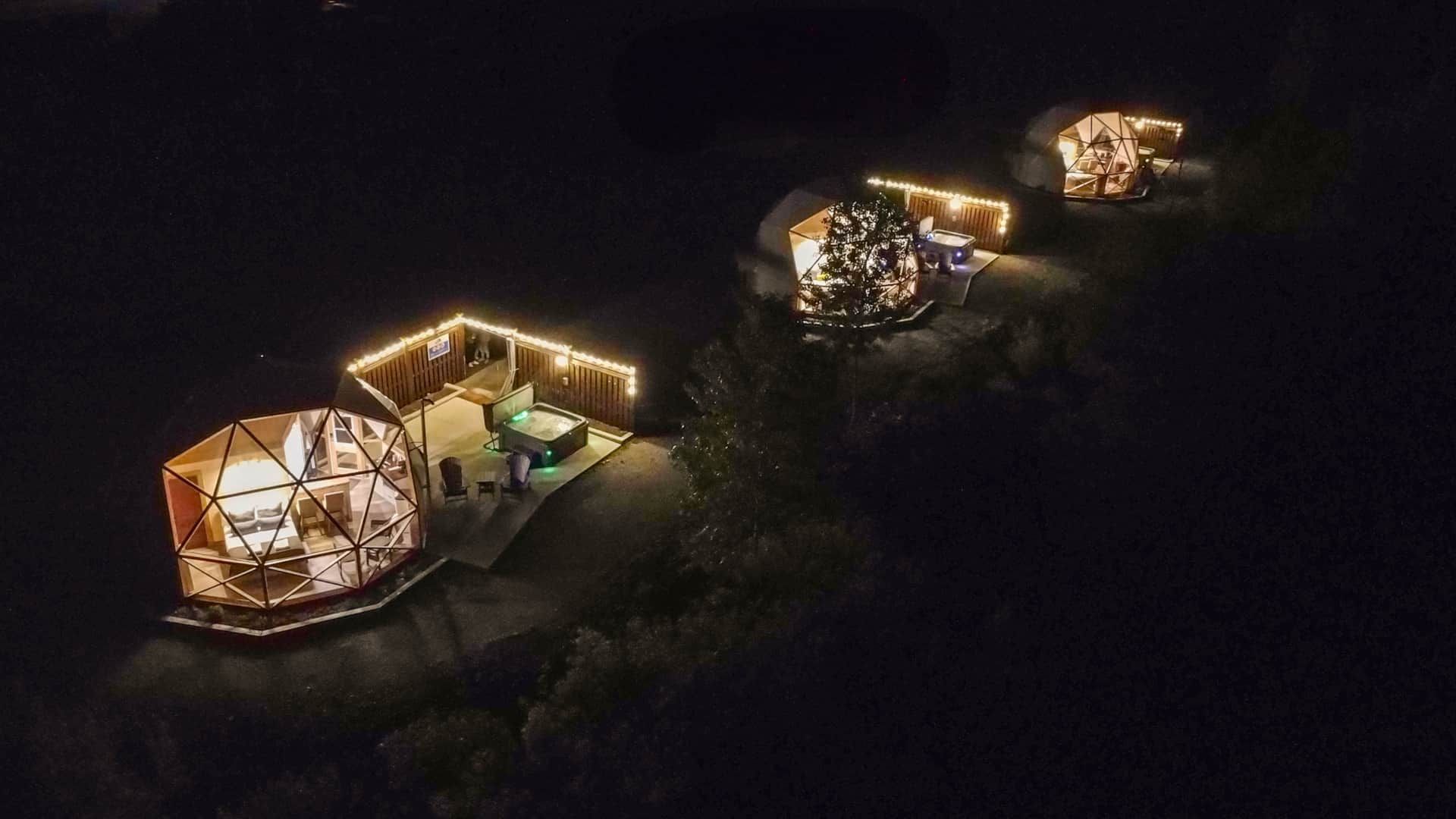 Luchtfoto 's nachts van drie oplichtende domes van Appalaches Domes in een open plek in het bos.