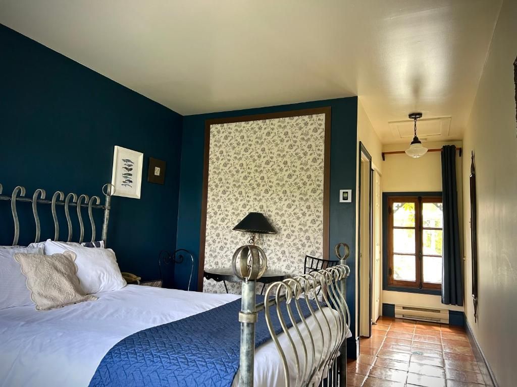 Slaapkamer met wit metalen bed, blauwe muren, een accentmuur met patroon en een gang naar een raam aan het uiteinde.