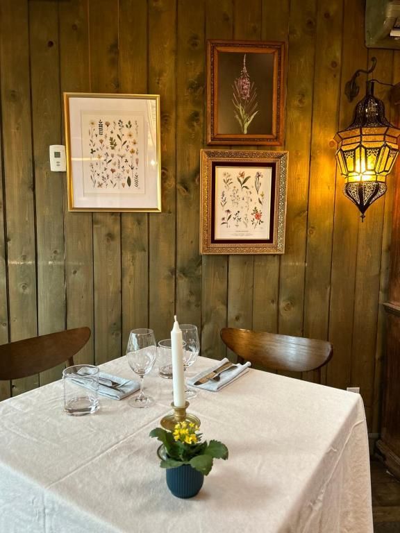 Gezellige, rustieke eettafel met wit tafelkleed, bloemen, ingelijste kunst en een warme wandlamp tegen een houten lambrisering.