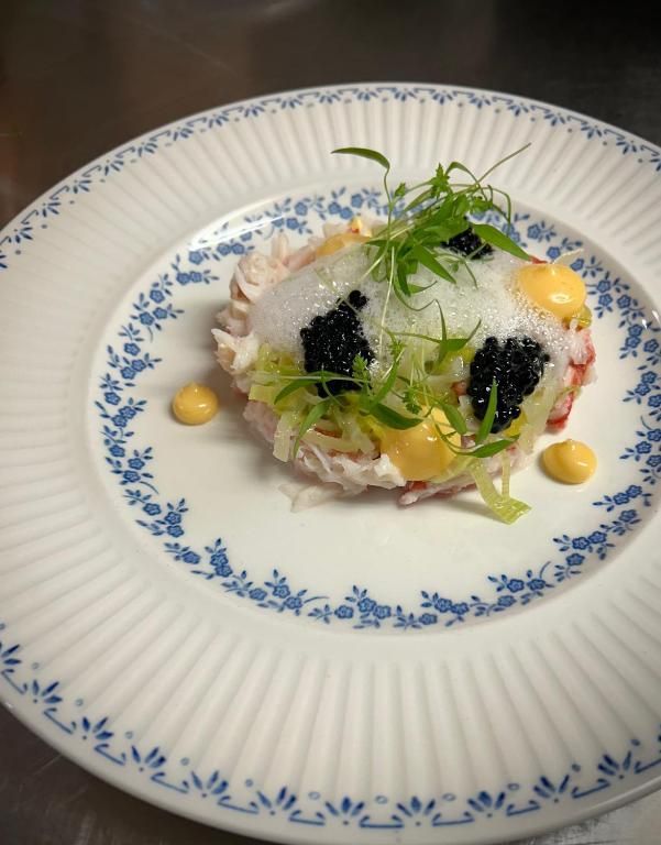 Een gastronomisch visgerecht op een wit bord met zwarte kaviaar, kruiden en een vleugje gele saus.