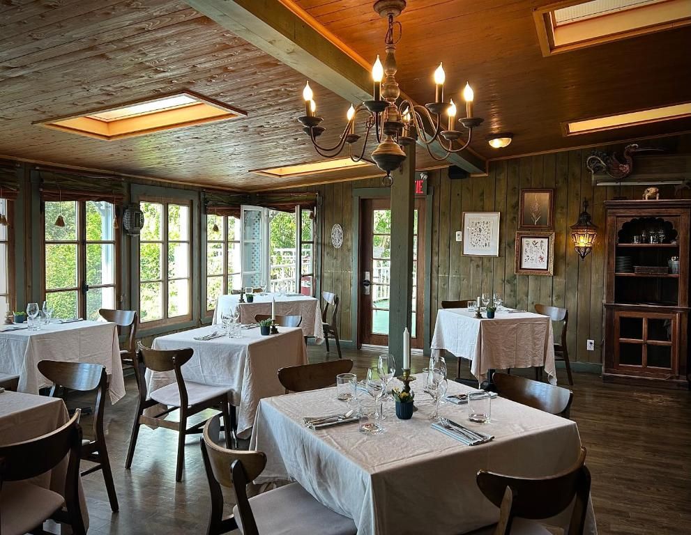 Gezellige, rustieke eetkamer met tafels met witte tafelkleden, houten stoelen, een kroonluchter en grote ramen.