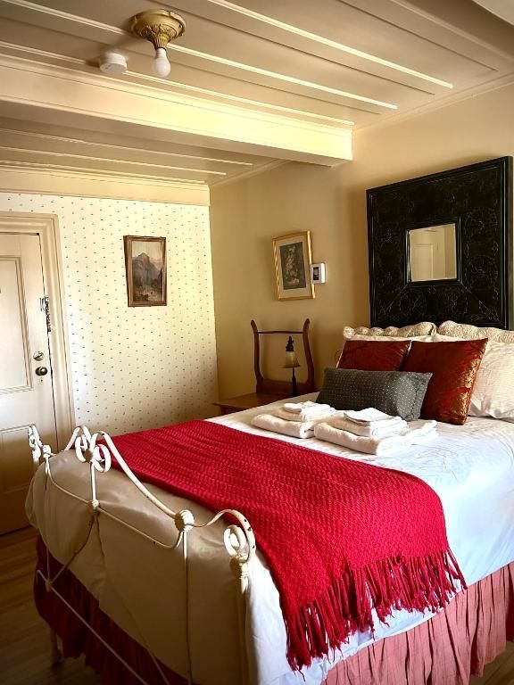 Gezellige slaapkamer met wit smeedijzeren bed, rode plaid en crèmekleurig behang, verlicht door warm natuurlijk licht.