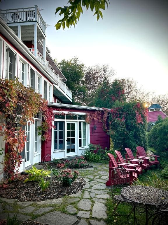 Stenen terras naast een wit huis met rode accenten, roze stoelen en met klimop begroeide muren in een tuinachtige omgeving.