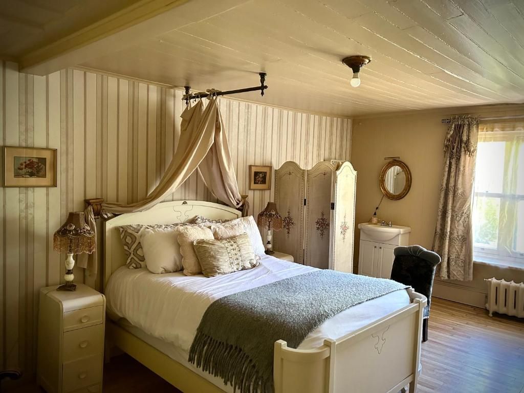 Gezellige slaapkamer met een hemelbed, bloemendecoratie, gestreept behang en zonlicht dat door het raam naar binnen schijnt.