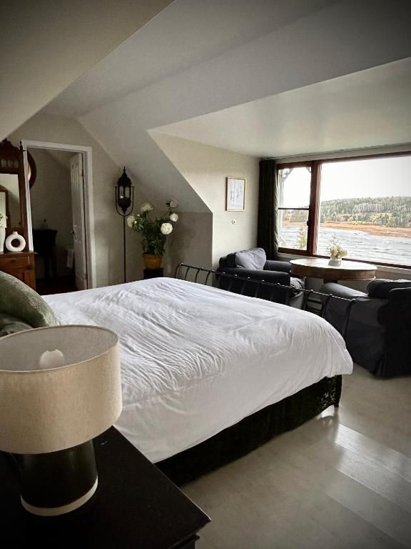 Lichte slaapkamer met wit bed, zwarte stoelen en een groot raam met uitzicht op het landschap.