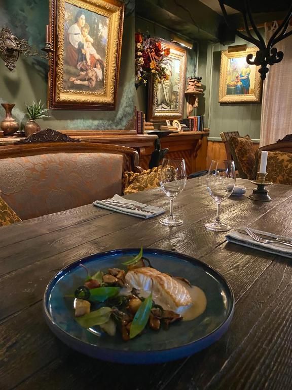 Gezellige eetzaal van een restaurant met een opgediend gerecht op de voorgrond en ingelijste schilderijen aan de muur.