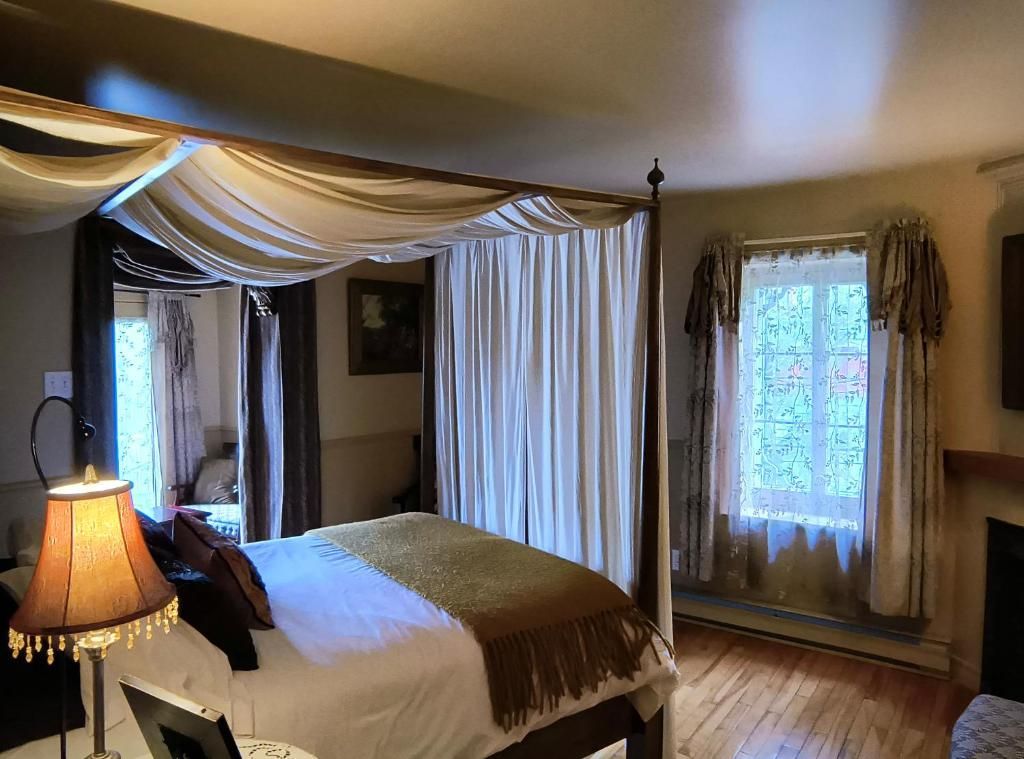 Gezellige slaapkamer met hemelbed, gedrapeerd baldakijn, lamp en raam met vitrage.
